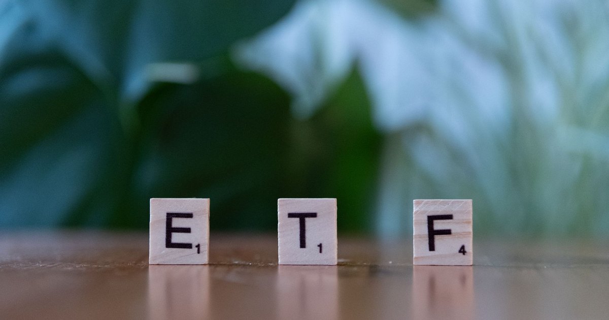 Scrabble tiles spelling ETF on a wooden surface with blurred green background.
