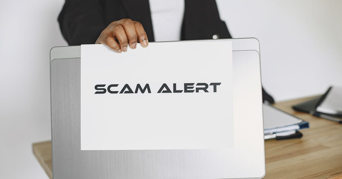 Business person holding a scam alert sign over a laptop, warning against online fraud.