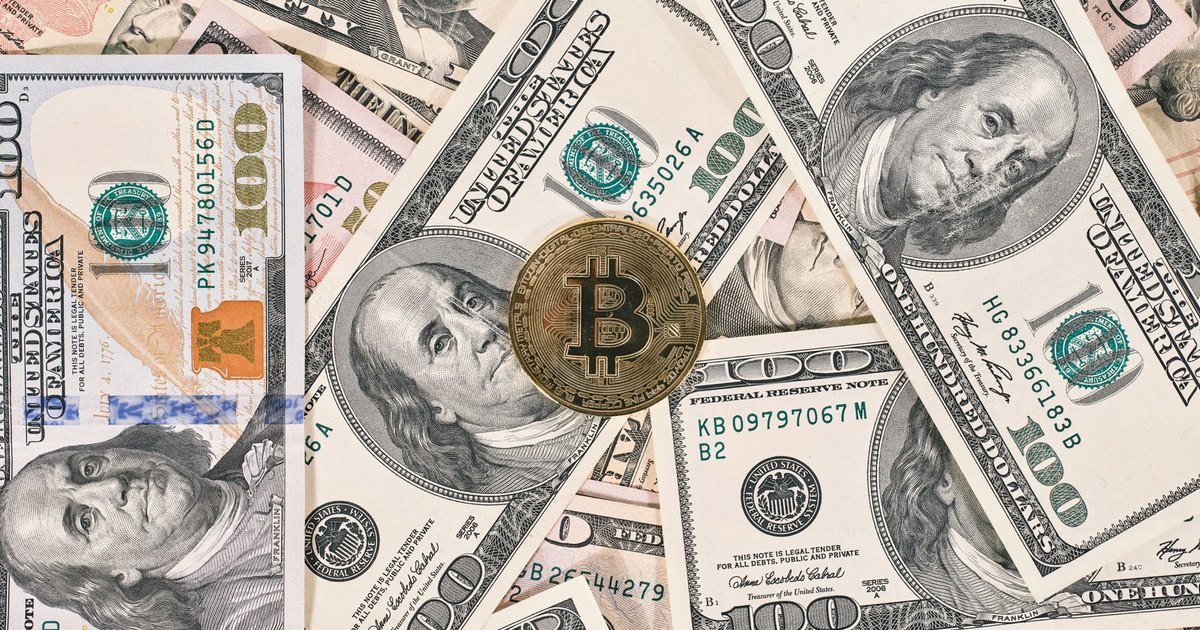 Bitcoin coin resting on a background of various US dollar bills, symbolizing the contrast between traditional and digital currency.
