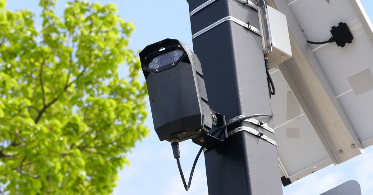 A modern surveillance camera powered by solar energy mounted on a street pole.