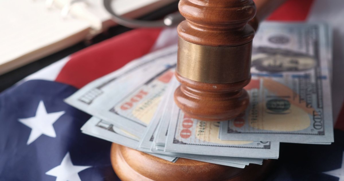 Close-up of a judge's gavel resting on US dollar bills and an American flag, symbolizing justice and finance.