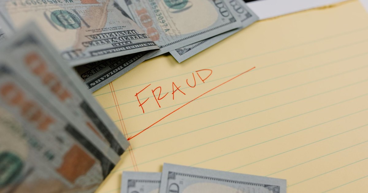 Close-up of US dollars and 'Fraud' written on yellow paper, representing financial scams.