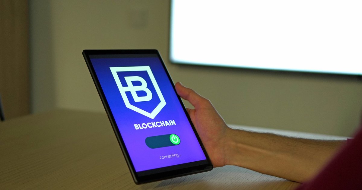 A hand holding a tablet with blockchain logo on screen, showcasing digital technology.