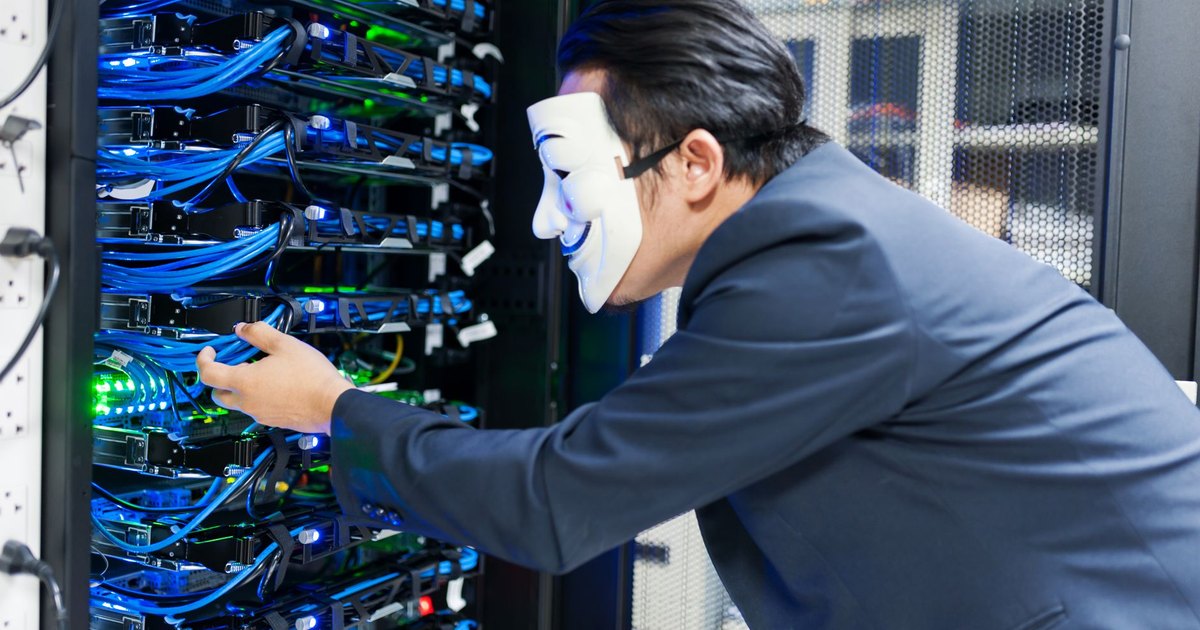 Masked individual interacting with server racks, symbolizing cybersecurity threats.