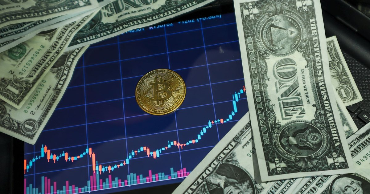 Bitcoin coin on a tablet showing stock chart, surrounded by dollar bills.