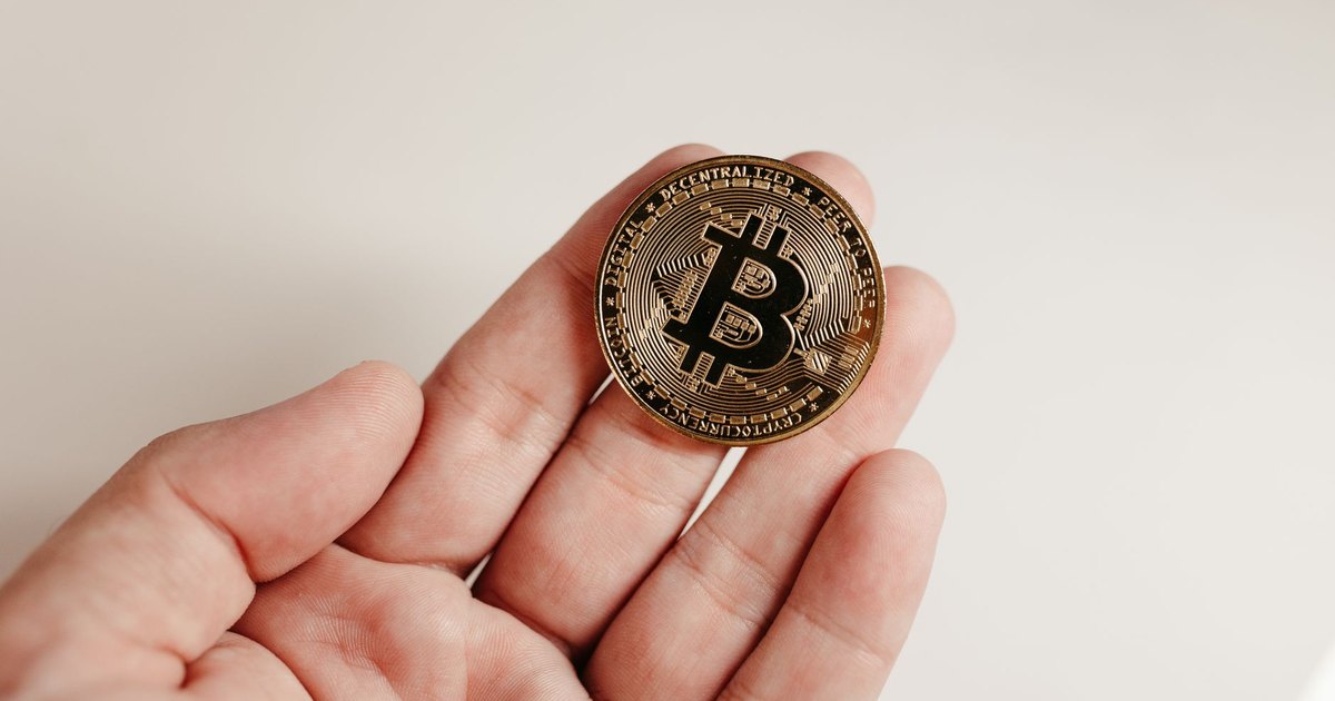 A close-up image of a Bitcoin coin held in a human hand against a white background.