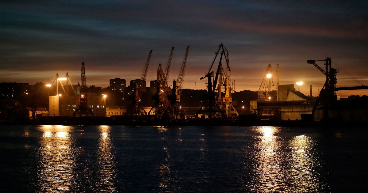 Night view of an illuminated industrial harbor with cranes reflecting on the water in Odesa, Ukraine.