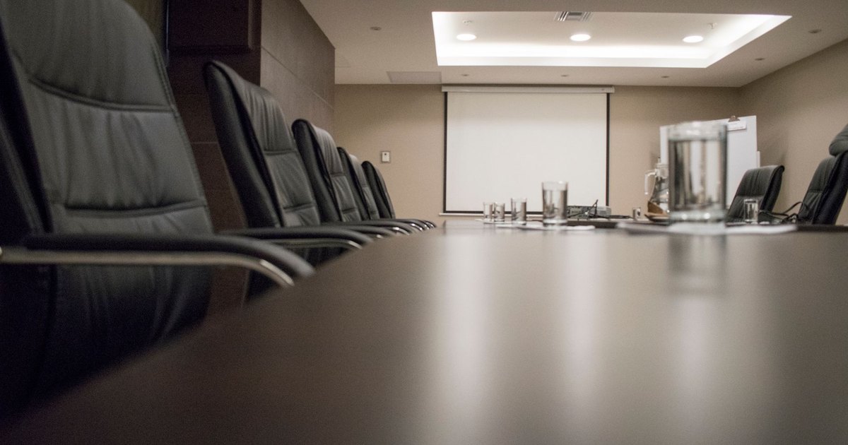 Empty conference room with black chairs, projector, and glasses on table. Ideal for business meetings.