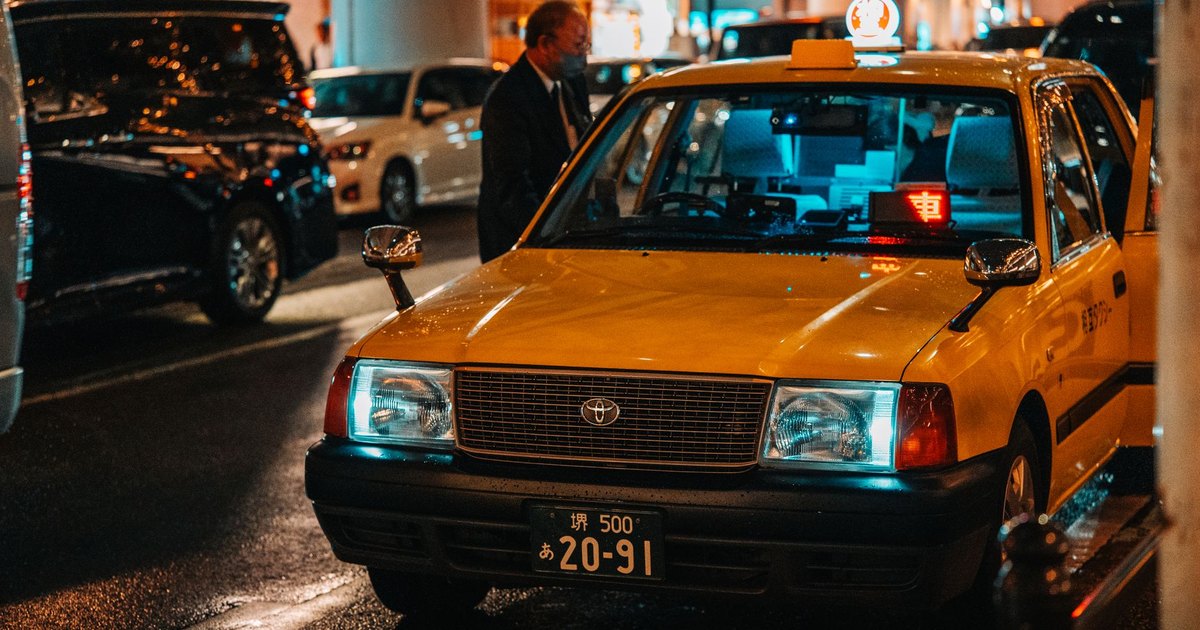 A vibrant night scene of a yellow taxi in Dotonbori, Osaka, capturing the city's lively atmosphere.