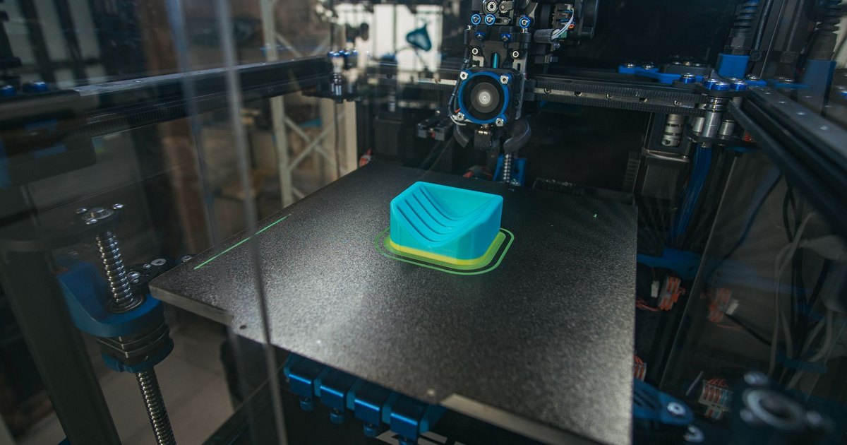 Close-up of a 3D printer creating a plastic object in an industrial setting.