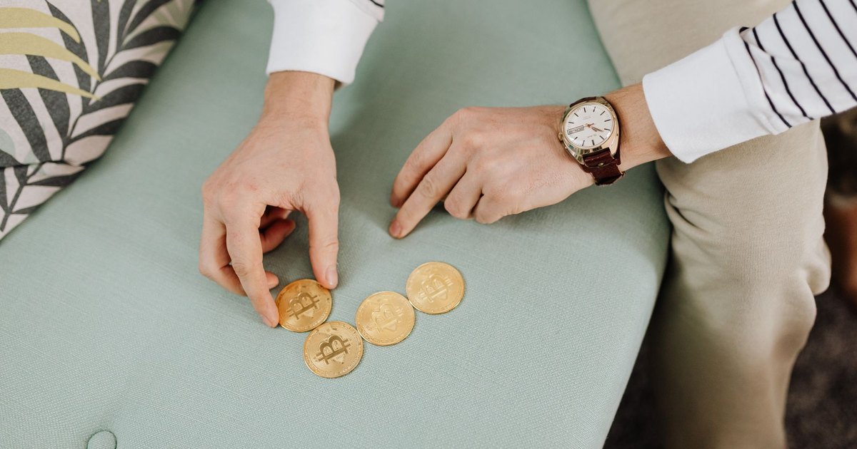 Close-up of hands holding bitcoin coins on a green sofa, emphasizing digital currency trends.