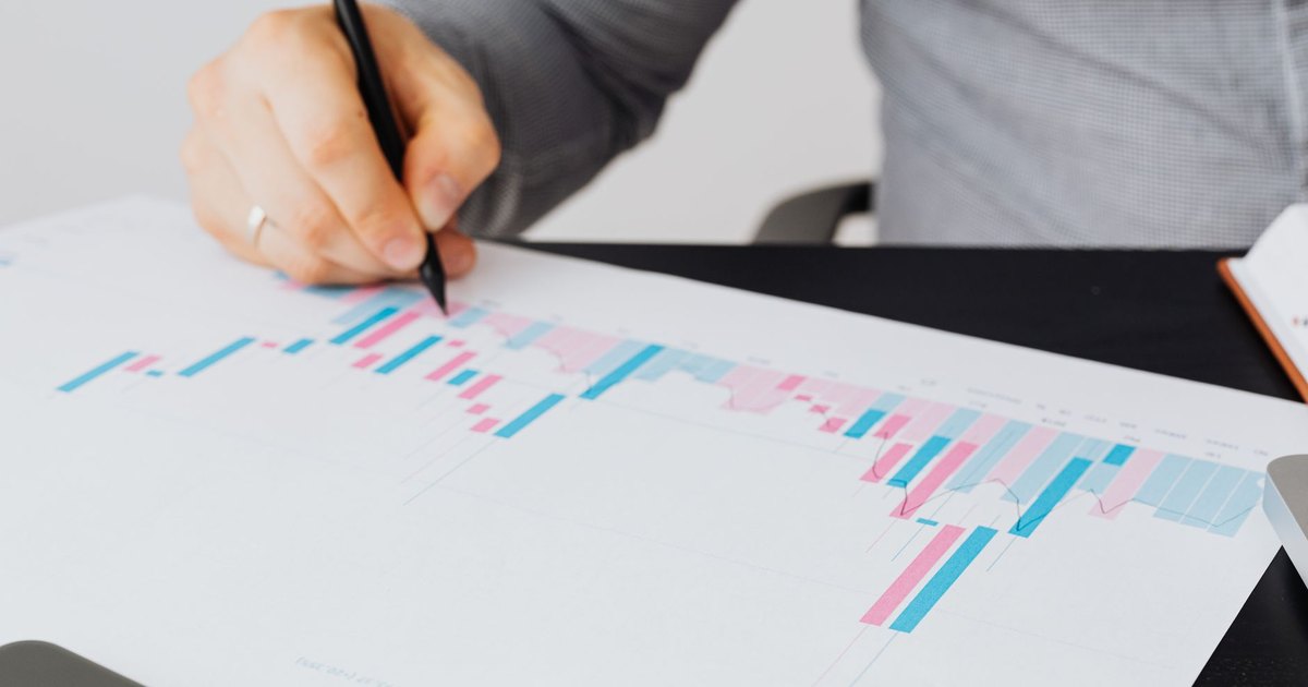 Close-up of a man writing on a printed chart indoors, analyzing colorful data.