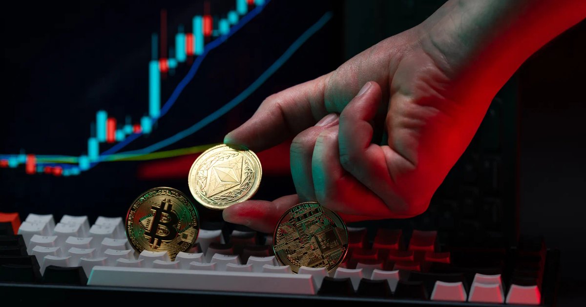 Close-up of a hand holding cryptocurrency coins on keyboard, with a graph display in the background.