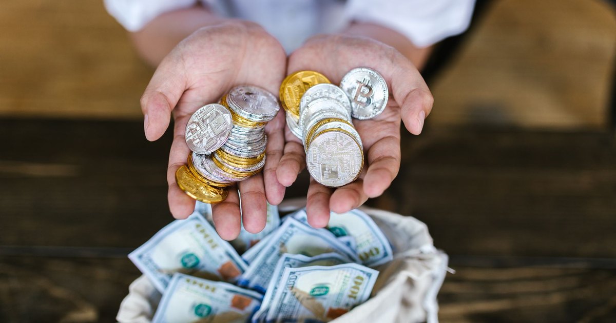 Person holding cryptocurrency coins above a bag of cash, symbolizing digital and traditional finance intersections.